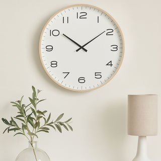 Modern clock up against a beige wall with a subtle plant