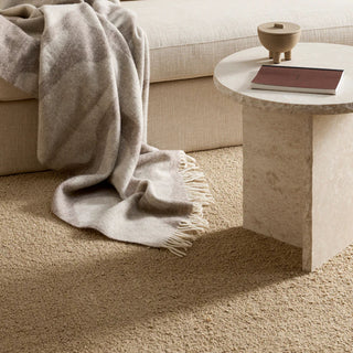 Beige carpet with a textured surface, a beige sofa, and a small round table with a book and decorative bowl.