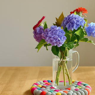 Glass vase with flowers sitting on a vibrant round felt potstand on a wooden table
