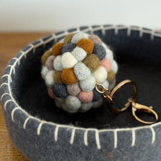 Neutral wool felt ball keyring resting inside a grey felt bowl