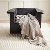 Dark wooden armchair with a beige blanket draped over it on a light wooden floor.