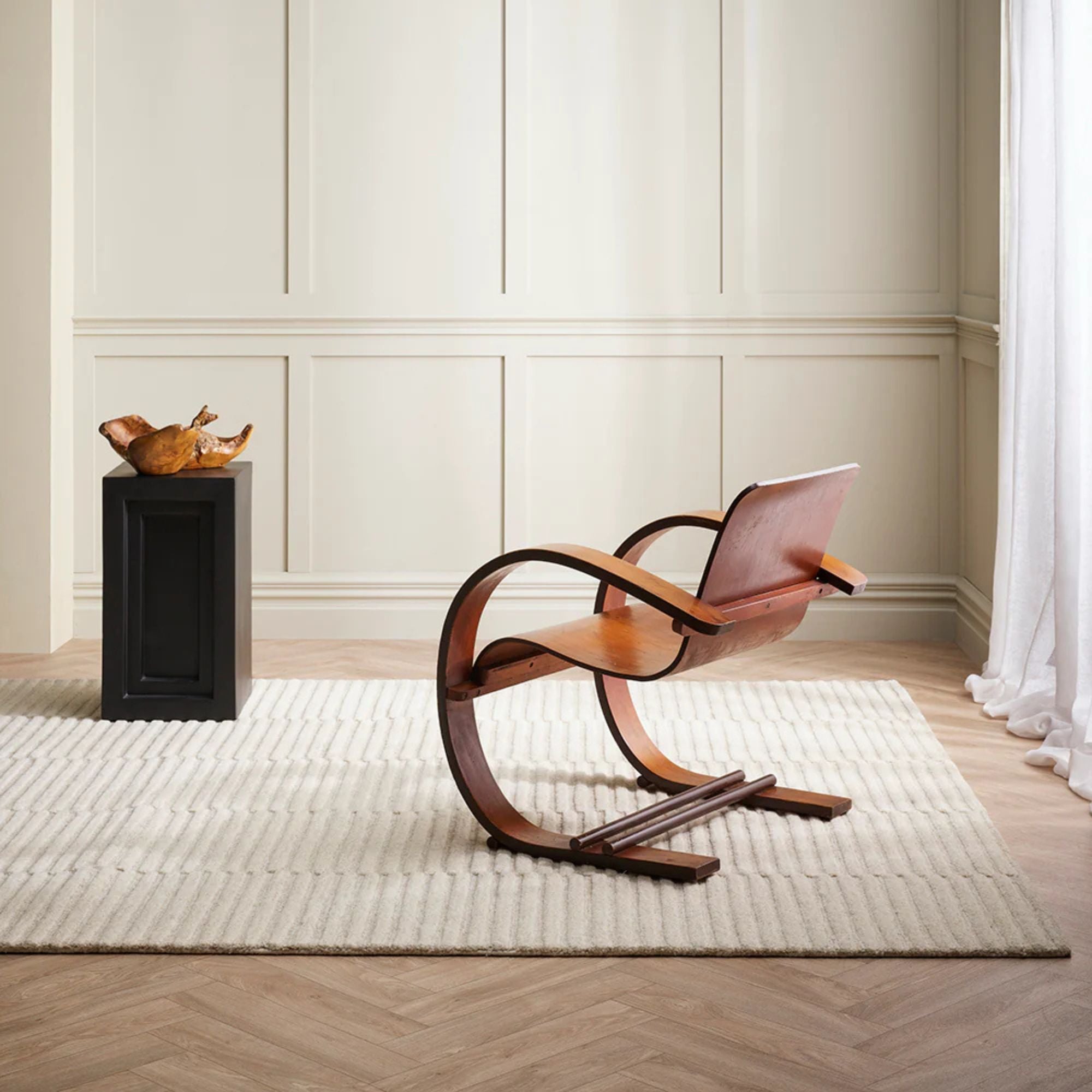 Modern wooden chair in a minimalistic room with white walls and wooden floor.