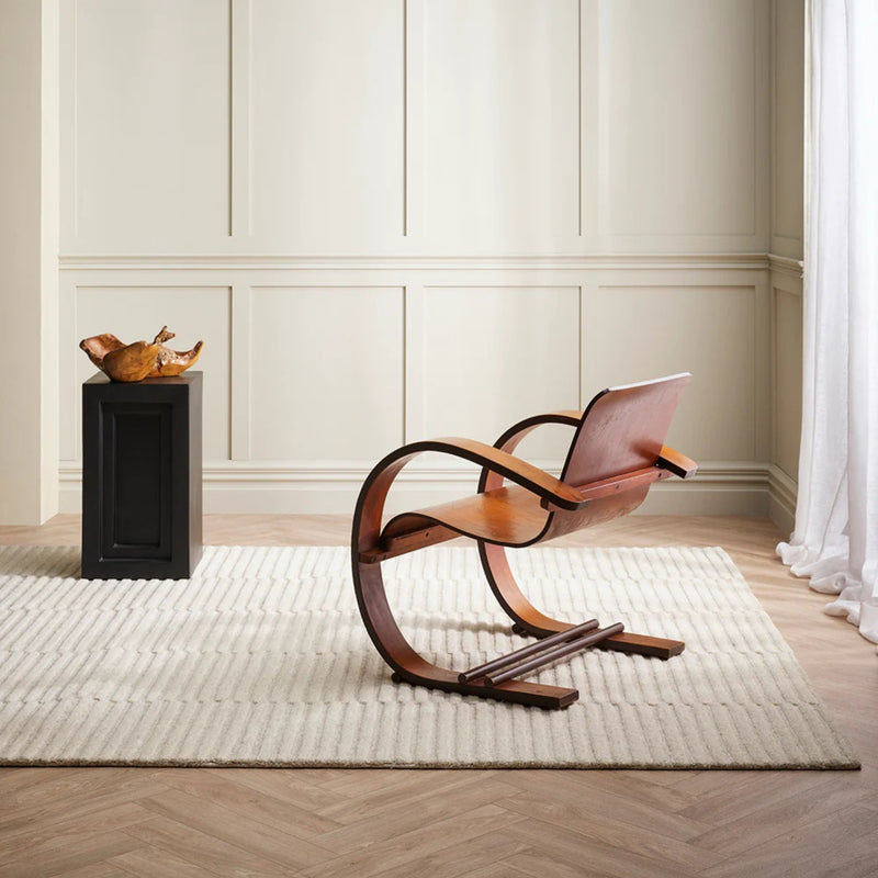Modern wooden chair in a minimalistic room with white walls and wooden floor.
