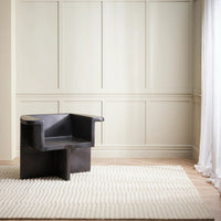 Modern black chair in a minimalistic room with white walls and a rug.