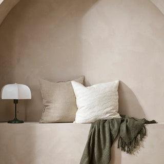 Two pillows on a ledge with a lamp and green blanket against a beige wall.