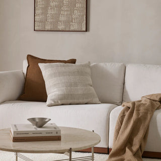 White sofa with brown and beige pillows and a blanket, coffee table with books and a bowl in a living room.
