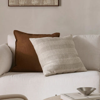White sofa with brown and gray patterned cushions, framed artwork on wall.