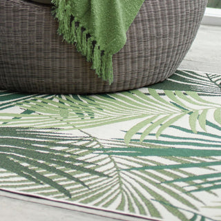 Green and white patterned rug with a wicker chair and green blanket.