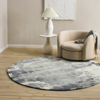 Round gray rug on a wooden floor with a beige armchair and white lamp in a room.