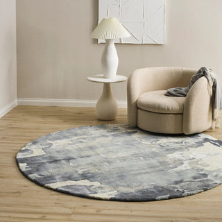 Round gray rug on a wooden floor with a beige armchair and white lamp in a room.