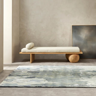 Minimalist wooden bench with white cushion on a gray rug in a room with a textured wall.