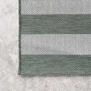 Close-up of a green and white striped rug on a concrete floor.