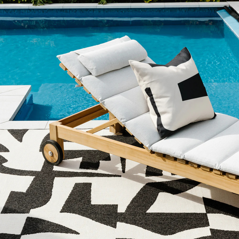Wooden lounge chair with white and black cushions by a pool