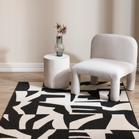 Modern interior with a black and white patterned rug, white textured chair, and round white table.