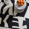 Black and white patterned rug with a bowl of oranges on a small table.