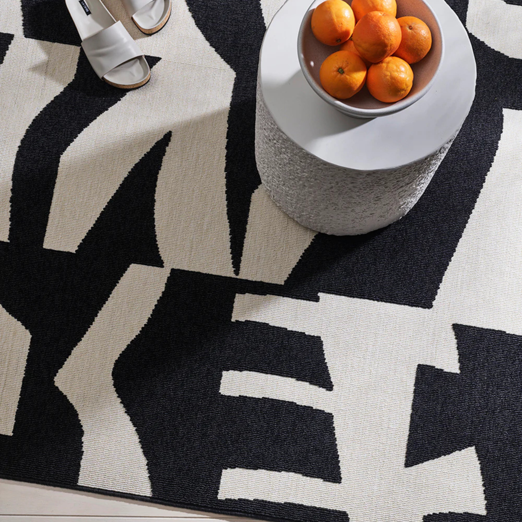 Black and white patterned rug with a bowl of oranges on a small table.