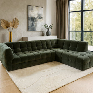 Green sectional sofa in a living room with a large window and abstract art on the wall.