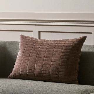 Quilted chocolate pillow on a gray sofa against a neutral wall.