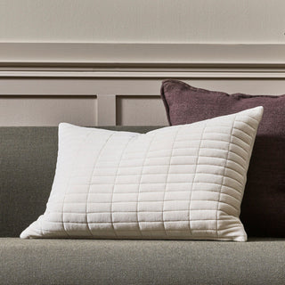 Quilted white pillow on a gray sofa with a purple pillow in the background.