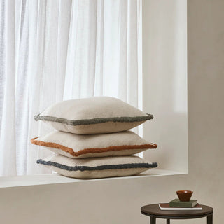 Stack of three decorative pillows on a windowsill with a neutral background