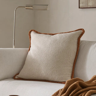 Beige pillow with brown trim on a beige sofa in a living room setting.