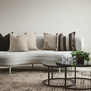 Modern living room with a curved white sofa adorned with patterned cushions, a black coffee table, and a plant.