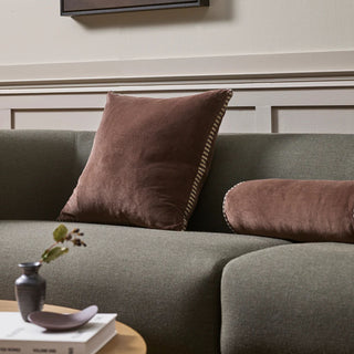 Gray sofa with brown cushions and a small table with books and a vase in a room.