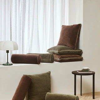 Decorative pillows on a white surface with a lamp and small table in the background.