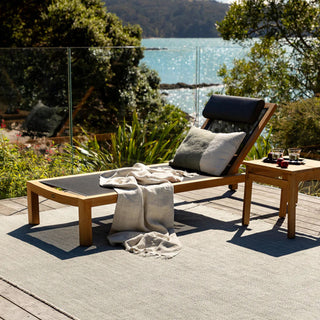Outdoor lounge chair with cushions on a deck overlooking a body of water.
