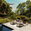 Two lounge chairs on a wooden deck overlooking a scenic ocean view with lush greenery.