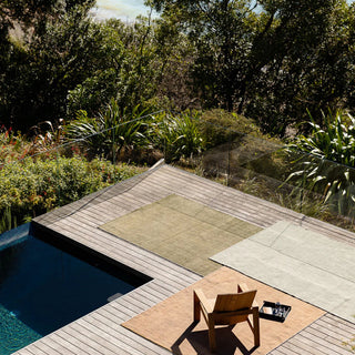 Outdoor setting with a pool, wooden deck, and chair surrounded by greenery.