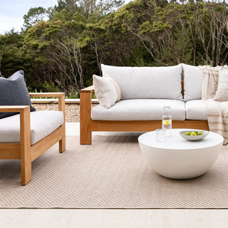 Outdoor furniture set with a sofa, chair, and coffee table on a patio with a natural background.