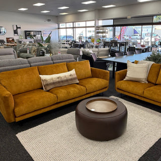 Living room with gold sofas, a round brown ottoman, and a rug.