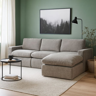 Grey sectional sofa in a living room with a green wall, framed picture, and small table.