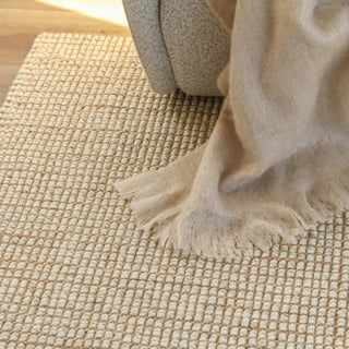 Close-up of a textured beige rug with a soft fabric draped over it.