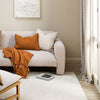 Living room with a beige sofa, orange throw blanket, and white rug.