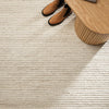 Close-up of a textured beige carpet with a wooden side table and shoes in the corner.
