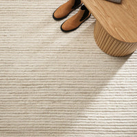 Close-up of a textured beige carpet with a wooden side table and shoes in the corner.
