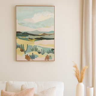 Abstract landscape wall art hanging above a cream sofa with neutral cushions, styled in a bright modern living room with a wooden side table and ceramic vases.