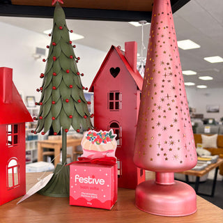 Decorative Christmas items including a pink lamp, green tree, and red houses on a table.