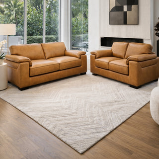 Brown leather sofa set in a modern living room with large windows and a rug.