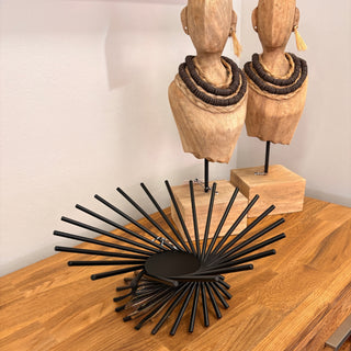 Black decorative item on a wooden surface with wooden mannequin heads in the background.