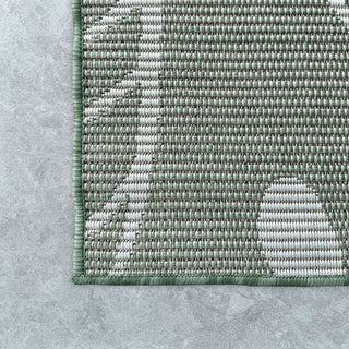 Close-up of a textured green and gray rug on a concrete floor.