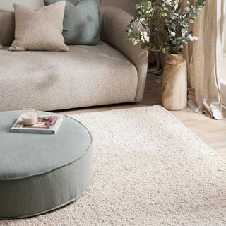 Living room with beige sofa, round ottoman, and decorative elements.