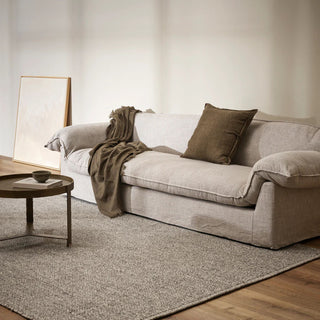 Beige sofa with a blanket and pillow in a living room setting