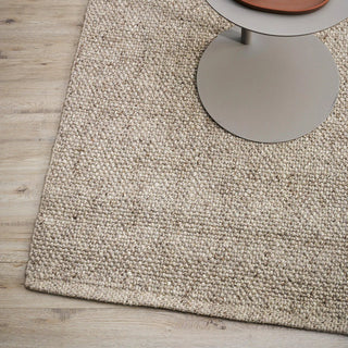 Beige textured rug on a wooden floor with a round metallic object partially visible.