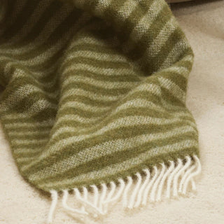 Green and white striped throw with fringes on a beige surface