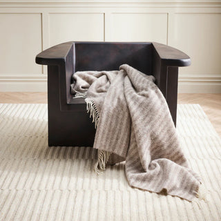 Dark wooden chair with a throw blanket draped over it on a light wooden floor.