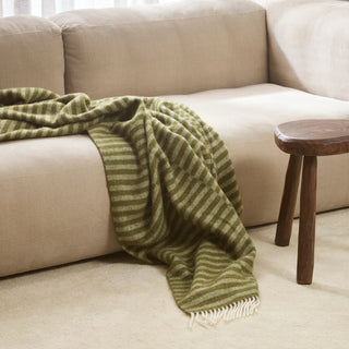 Green striped blanket throw over a beige sofa with a wooden side table in a living room setting.