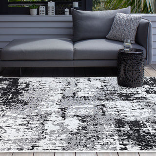 Gray outdoor sofa with patterned cushions on a black and white abstract rug.